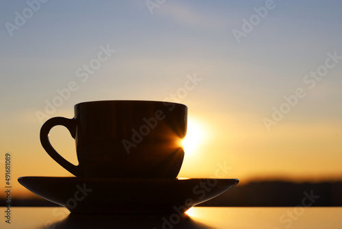 Silhouette of coffee or tea cup on sunrise sky background. View from the window to morning city