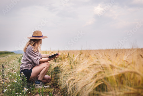Farmer working in barley field and examining quality of produce before harvest. Woman using digital tablet for smart farming