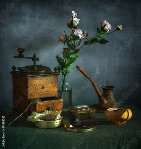 Still life with a bouquet of flowers, a cup of coffee, an old coffee grinder and a smoking pipe. Vintage.