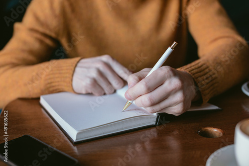Close up of man writing in blank notebook. Man working and drinking coffee in a cafe.