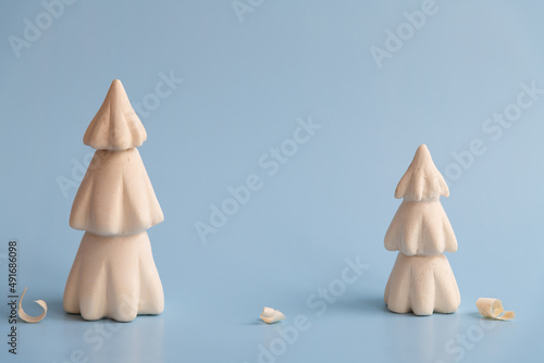 Handmade wooden carved Christmas trees with few shavings stands on blue background. Copy space for your text. Winter decoration theme.