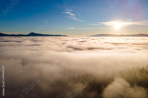 Aerial view of vibrant sunset over white dense clouds with dark mountain spruce forest trees.