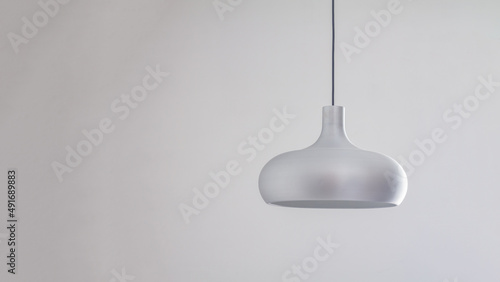 A silver metal lamp in a simple semicircular shape hangs on the ceiling against a gray wall background
