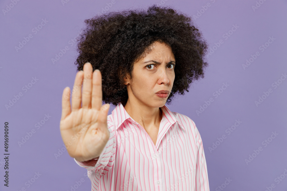 Young serious trict angry sad woman of African American ethnicity 20s wear pink striped shirt showing stop gesture with palm refusing isolated on plain pastel light purple background studio portrait Young serious trict angry sad woman of African American ethnicity 20s wear pink striped shirt showing stop gesture with palm refusing isolated on plain pastel light purple background studio portrait