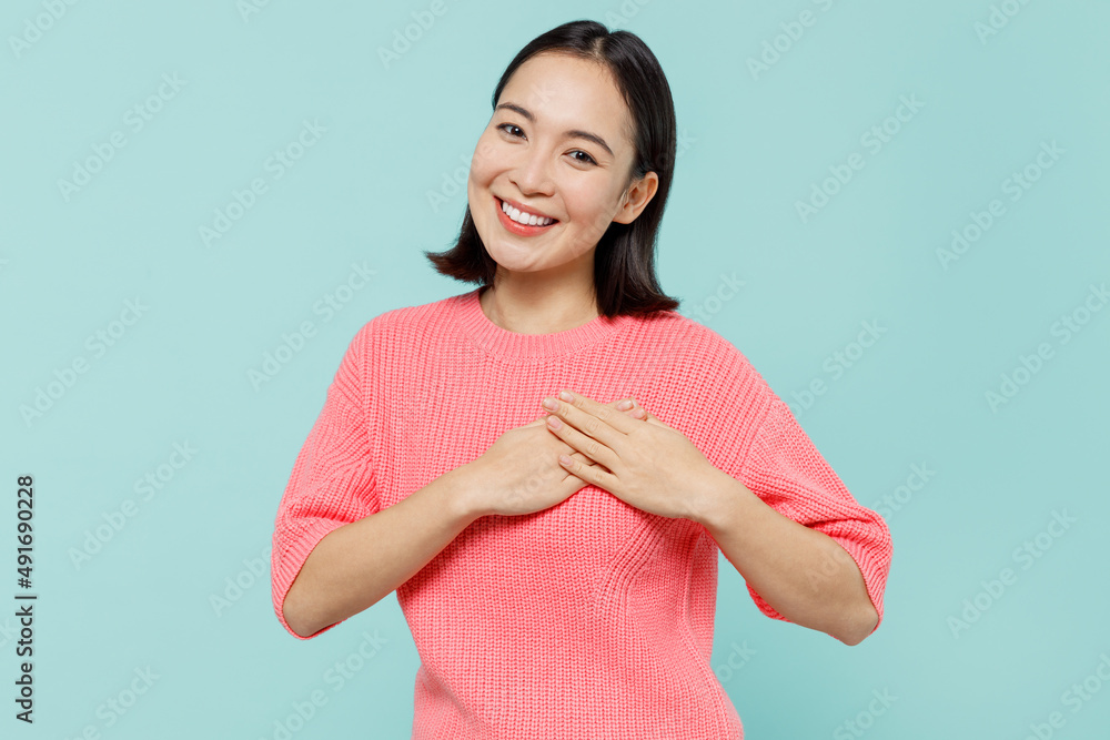 Young smiling kind-hearted happy woman of Asian ethnicity 20s in pink sweater put folded hands on heart isolated on pastel plain light blue color background studio portrait. People lifestyle concept Young smiling kind-hearted happy woman of Asian ethnicity 20s in pink sweater put folded hands on heart isolated on pastel plain light blue color background studio portrait. People lifestyle concept