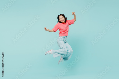 Full size young excited happy woman of Asian ethnicity 20s wearing pink sweater jump high do winner gesture isolated on pastel plain light blue background studio portrait. People lifestyle concept