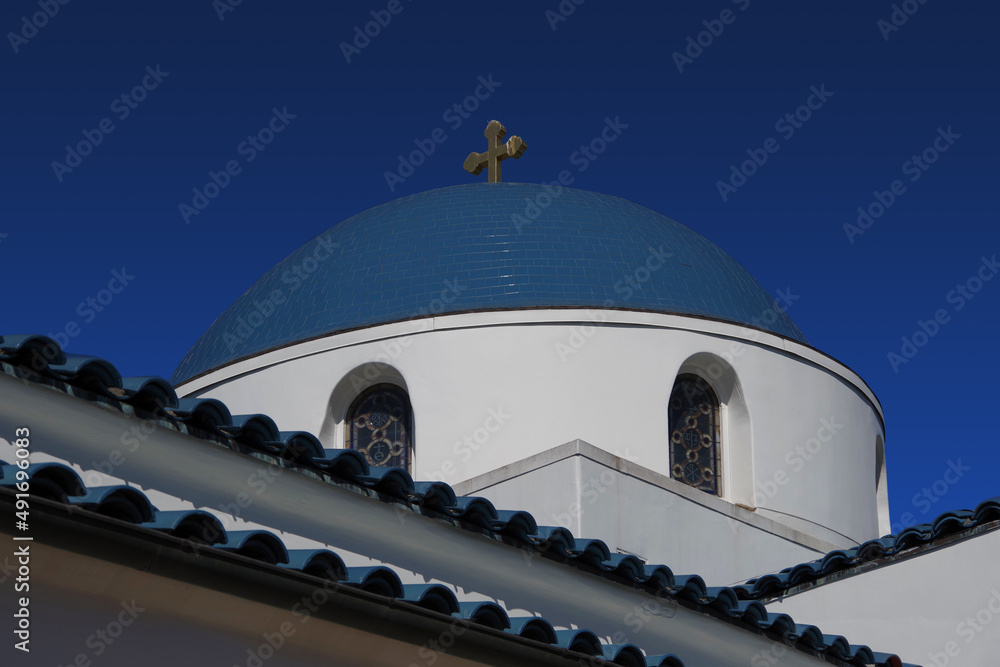 Dome of white Greek Orthodox church with blue roof and blue sky