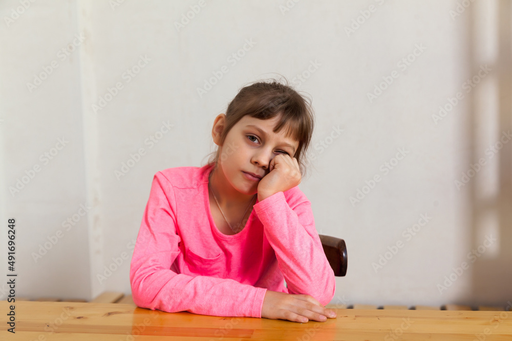 Unhappy little girl nine years old sitting at table Unhappy little girl nine years old sitting at table