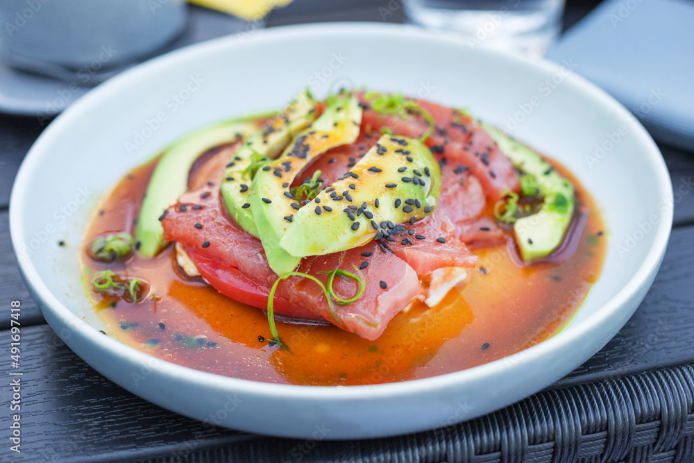 Close up fresh tuna fillet served with avocado, fresh tomato and sauce and garnished with black sesame seeds on wooden table. Healthy eating. Flexitarian diet. Close up fresh tuna fillet served with avocado, fresh tomato and sauce and garnished with black sesame seeds on wooden table. Healthy eating. Flexitarian diet.