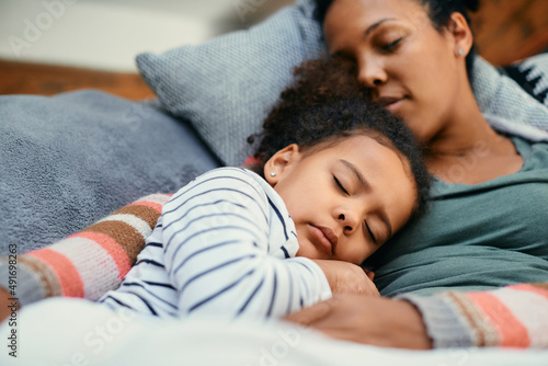 Embraced black mother and daughter taking a nap on sofa at home. photo