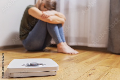 White scales and depressed, upset and sad woman sitting on wooden floor