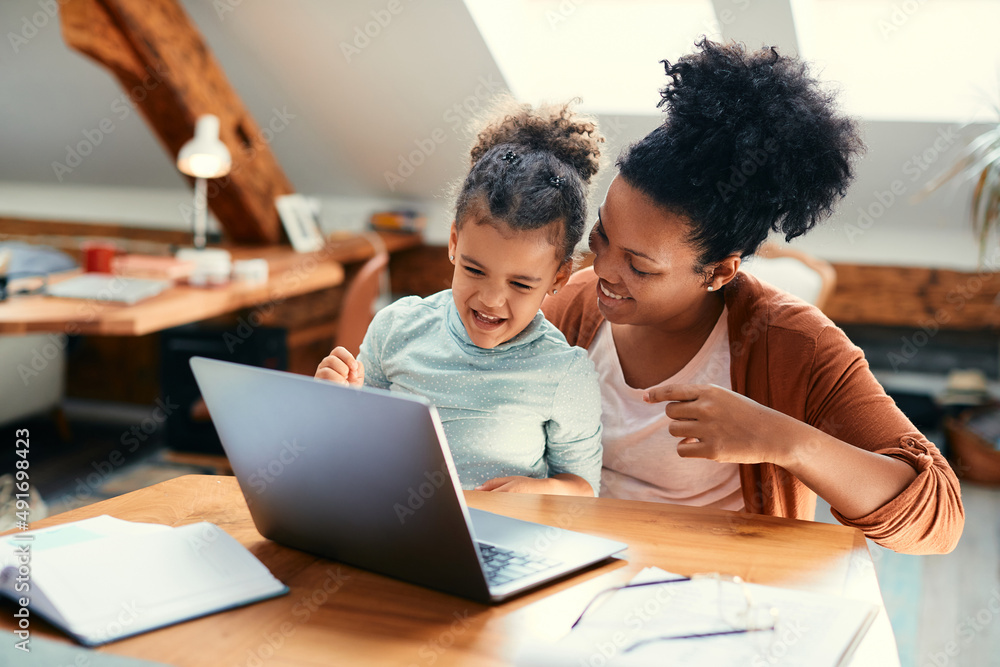 Cheerful black mother and daughter have fun while using laptop at home. Cheerful black mother and daughter have fun while using laptop at home.