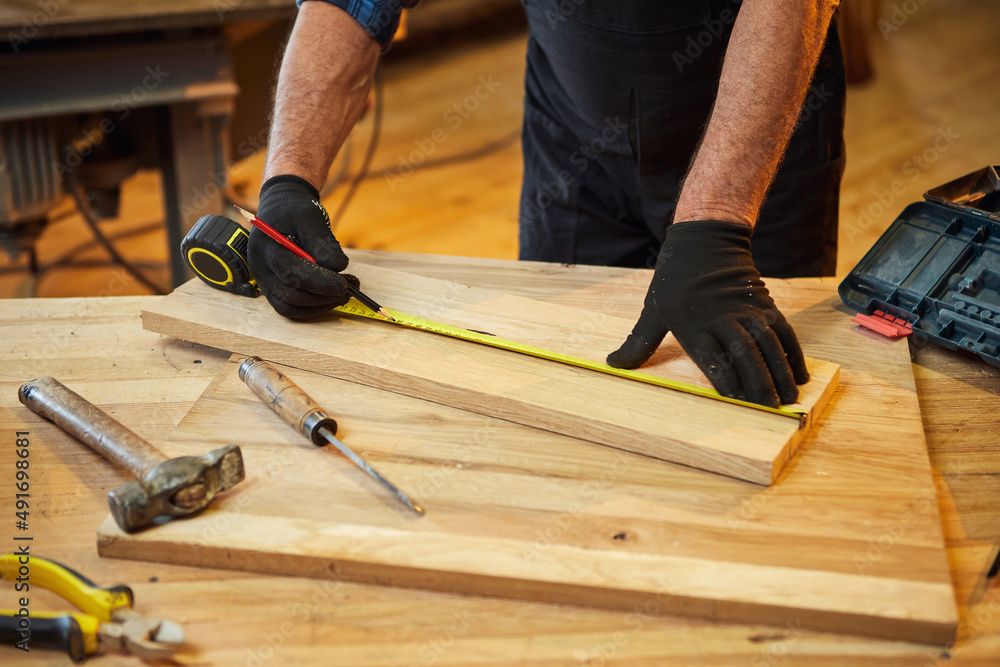 Carpenter working with a wood, marking plank with a pencil and taking measurements to cut a piece of wood to make a piece of furniture in a carpentry workshop, close-up view