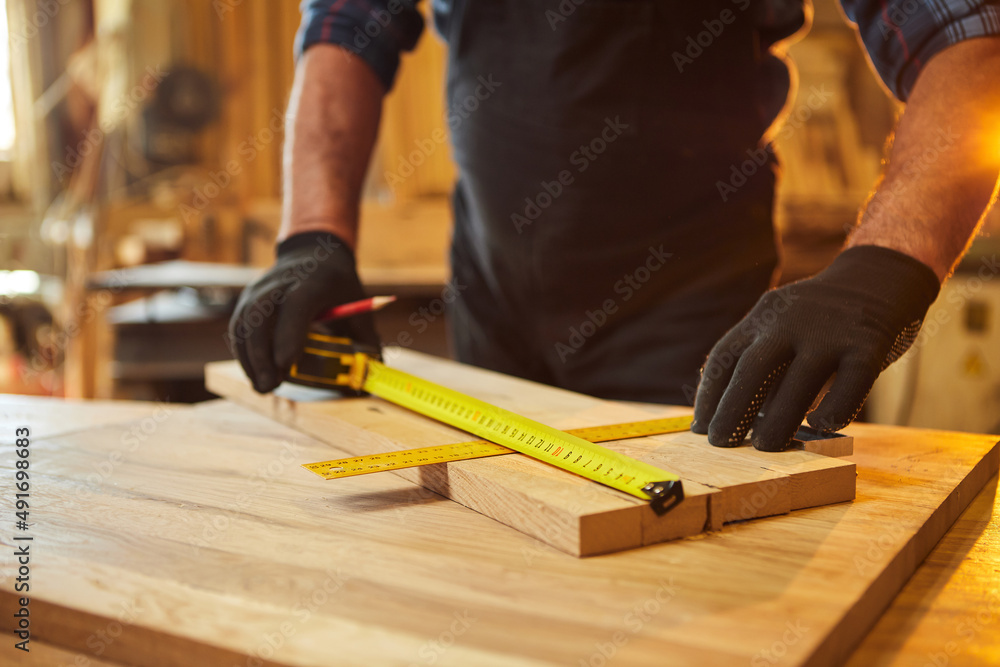 Carpenter working with a wood, marking plank with a pencil and taking measurements to cut a piece of wood to make a piece of furniture in a carpentry workshop, close-up view Carpenter working with a wood, marking plank with a pencil and taking measurements to cut a piece of wood to make a piece of furniture in a carpentry workshop, close-up view