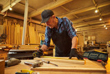 Portrait of a senior carpenter working with a wood, marking plank with a pencil and taking measurements to cut a piece of wood to make a piece of furniture in the carpentry workshop