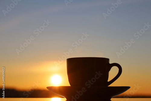 Silhouette of coffee or tea cup on sunset sky background. View from the window to evening city