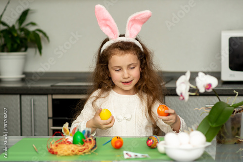 A girls in hare ears paints eggs. Easter. She is at home in the kitchen. Preparation for the holiday.