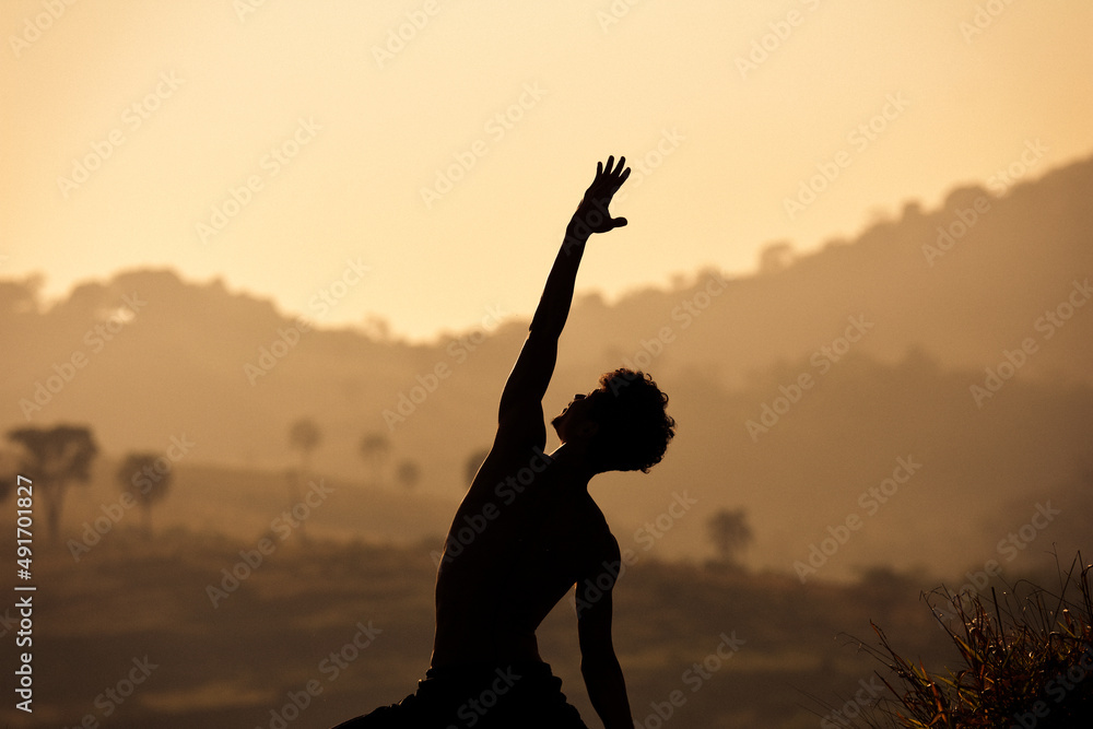 Young man doing yoga at the red orange sunset in the hills landscape