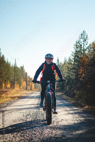 Young likeable lady with a lovely realistic smile while recreationally sporting. Cyclist riding fat bike in Finnish wild nature. Vuokatti area. Cycling clothing and helmet
