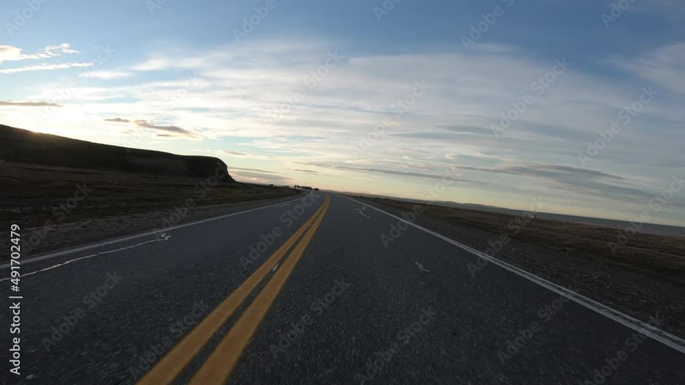 Freedom. Point of view of a car driving along the desert road at sunset. The yellow grassland and hills besides the route. The hiding sun in the horizon creates a beautiful lens flare. Freedom. Point of view of a car driving along the desert road at sunset. The yellow grassland and hills besides the route. The hiding sun in the horizon creates a beautiful lens flare.
