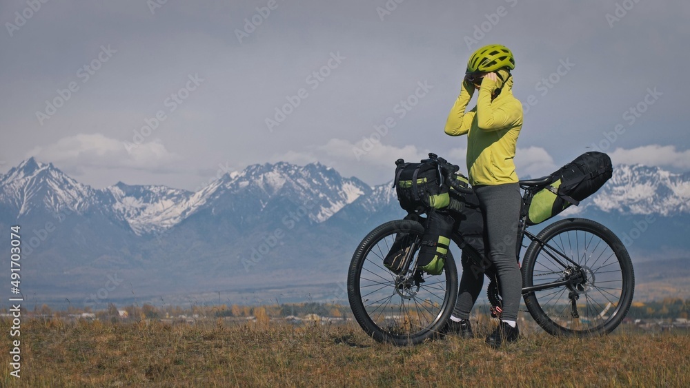The woman travel on mixed terrain cycle touring with bikepacking. The traveler journey with bicycle bags. Sport tourism bikepacking, bike, sportswear in green black colors. Mountain snow capped. The woman travel on mixed terrain cycle touring with bikepacking. The traveler journey with bicycle bags. Sport tourism bikepacking, bike, sportswear in green black colors. Mountain snow capped.