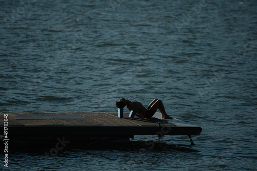 Young man doing yoga in a pier over the sea with beautiful mountains behind