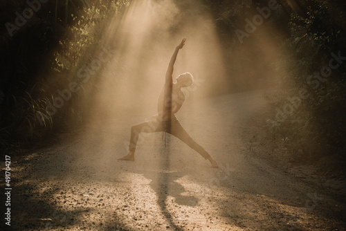 Young man doing yoga dance in the nature with a beautiful fog light in the middle of the light rays 