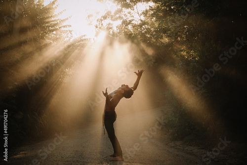 Young man doing yoga dance in the nature with a beautiful fog light in the middle of the light rays  #491704276
