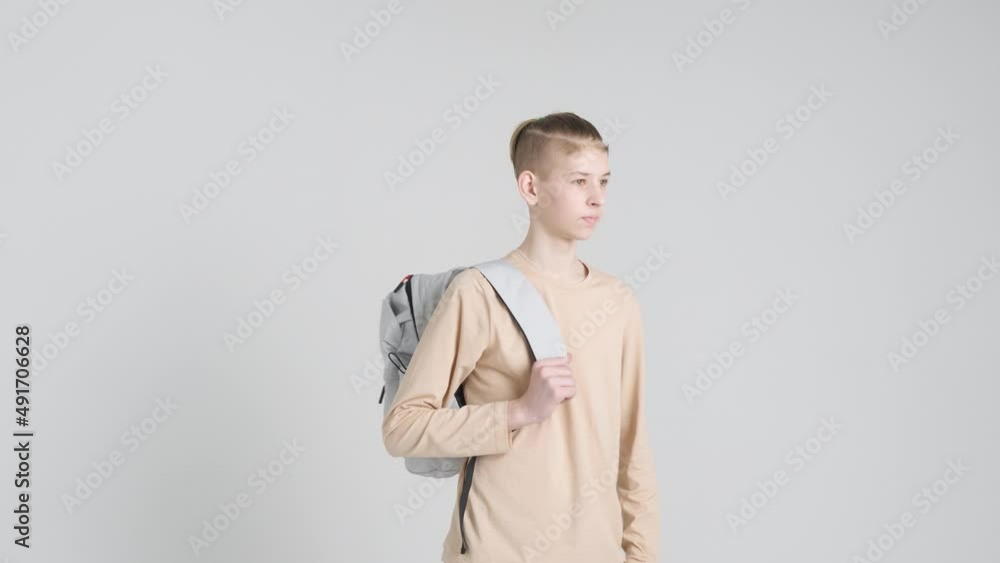 Happy boy teenager in beige clothes with gray backpack behind his back smiles at the camera on a white background. Back to school Happy boy teenager in beige clothes with gray backpack behind his back smiles at the camera on a white background. Back to school