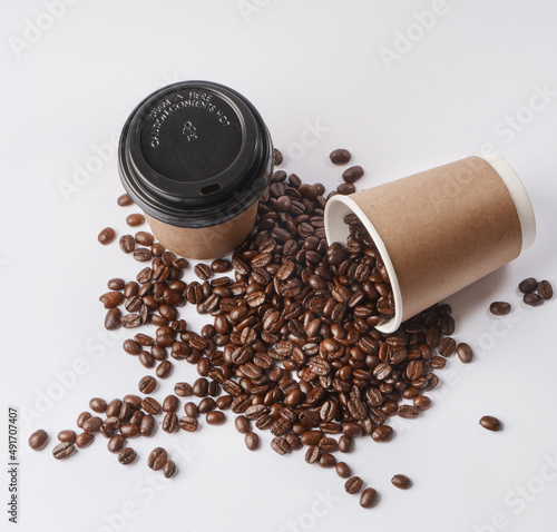 Start with Coffee. Studio shot of a tipped over paper cup filled with coffee beans against a grey background.