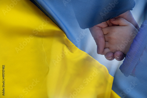 Fotografie, Obraz Mother holds a little girl by the hand against the background of the national flag of Ukraine yellow-blue