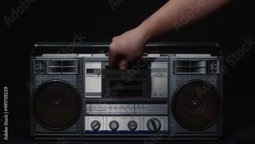 A man's hand inserts a cassette into an old vintage cassette recorder and presses the play button