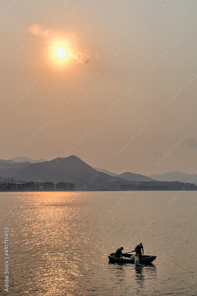 Two men in a boat fishing at sunset on Tolo Harbour, Ma On Shan, Hong Kong.