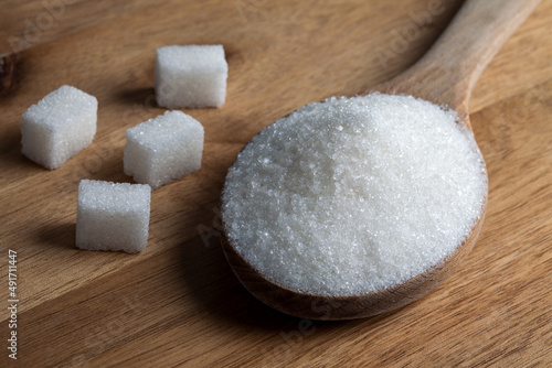 Granulated sugar and sugar cubes in wooden spoon on wooden background	