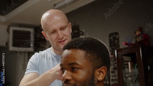 Caucasian hairdresser combing brown curly hair to young african american man