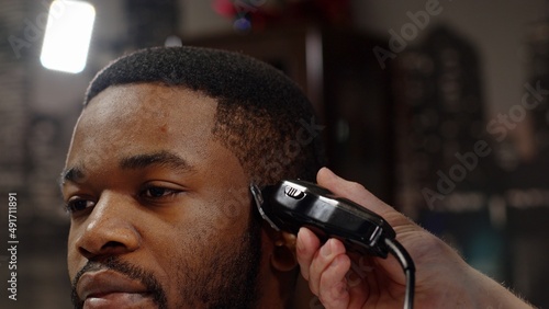 White guy doing a haircut to a young joyful african american guy in a beautiful barbershop photo