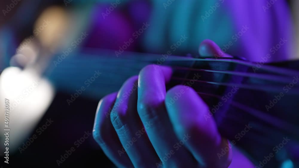 Hand of woman touching strings of guitar performing on stage illuminated by dark purple light. Musician enjoys playing musical instrument extreme closeup Hand of woman touching strings of guitar performing on stage illuminated by dark purple light. Musician enjoys playing musical instrument extreme closeup