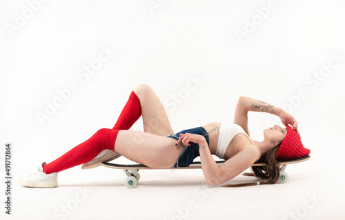 skater girl lying on a longboard in bright fashionable clothes on a white background