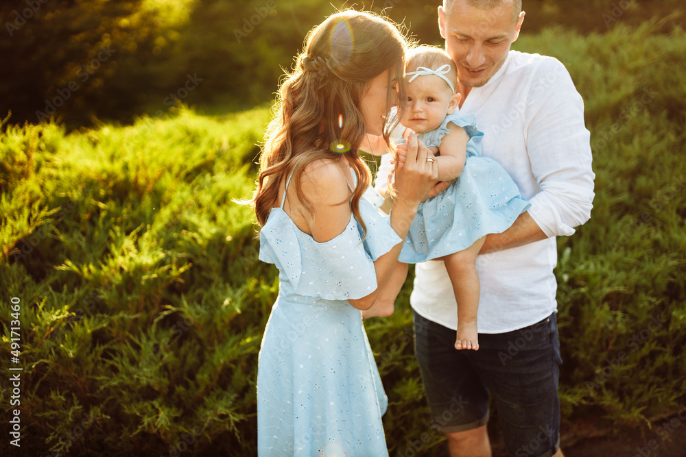 Obraz premium Little cute baby girl with mom and dad, beautiful daughter sitting on strong fathers arms and smile to caring mother, happy young family at the park