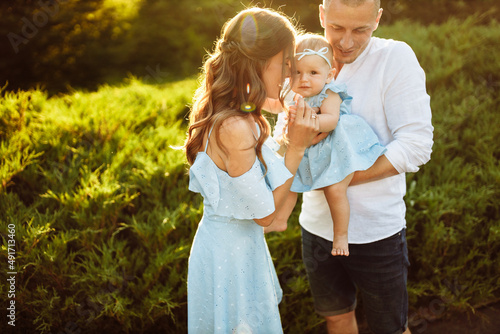 Little cute baby girl with mom and dad, beautiful daughter sitting on strong fathers arms and smile to caring mother, happy young family at the park © shunevich