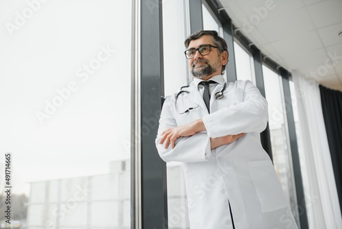 Happy confident bearded old professional doctor standing. Smiling senior adult physician, reliable successful therapist wearing white lab coat and stethoscope, portrait.