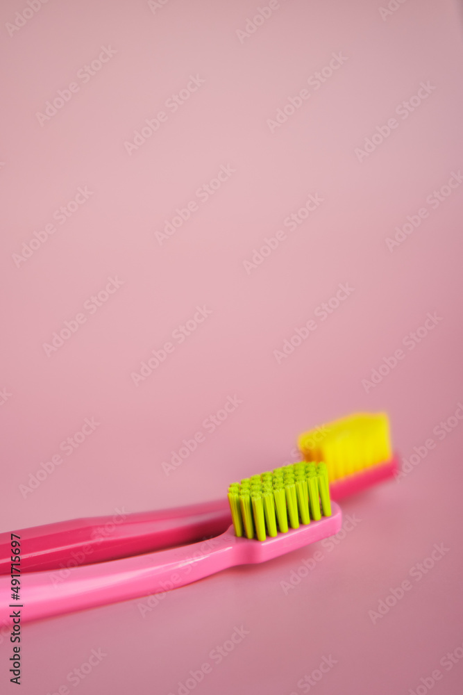 Two pink toothbrushes stand in pink glass on pink background. One brush is new and other has been used. Yellow bristles are disheveled, green bristles are new. Two pink toothbrushes stand in pink glass on pink background. One brush is new and other has been used. Yellow bristles are disheveled, green bristles are new.
