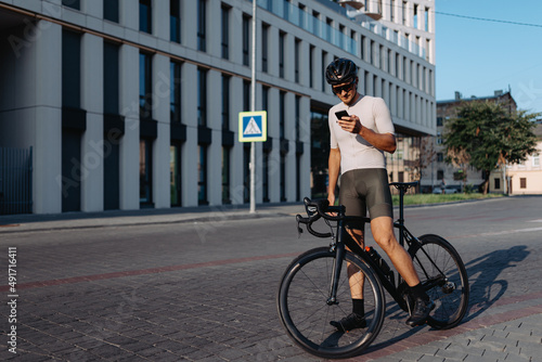 Cyclist standing on street with bike and using smartphone