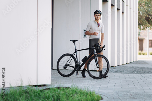 Cyclist in sportswear posing with bike near modern building.