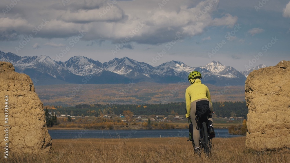 Obraz premium The woman travel on mixed terrain cycle touring with bikepacking. The traveler journey with bicycle bags. Sport bikepacking, bike, sportswear in green black colors. Mountain snow capped, stone arch.