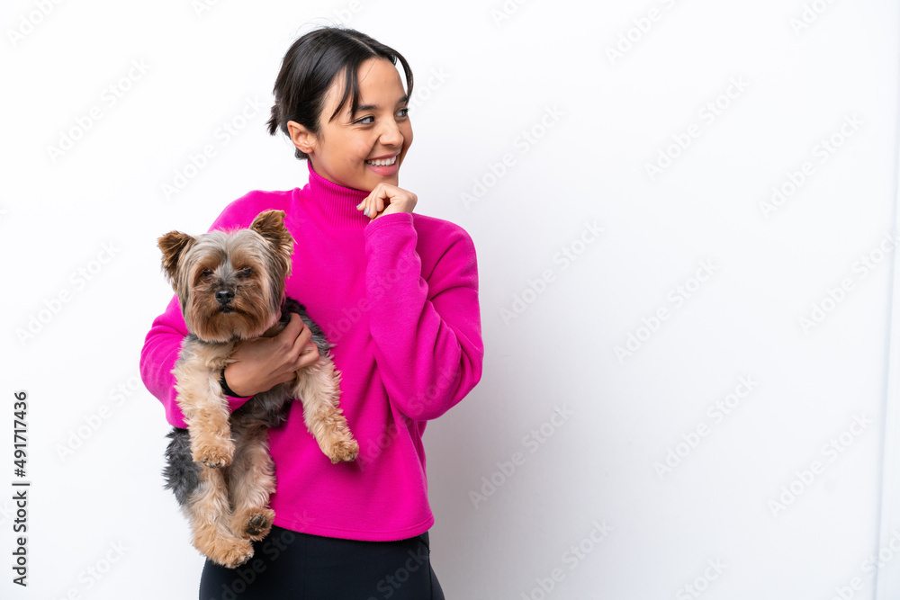 Young hispanic woman holding a dog isolated on white background thinking an idea and looking side Young hispanic woman holding a dog isolated on white background thinking an idea and looking side