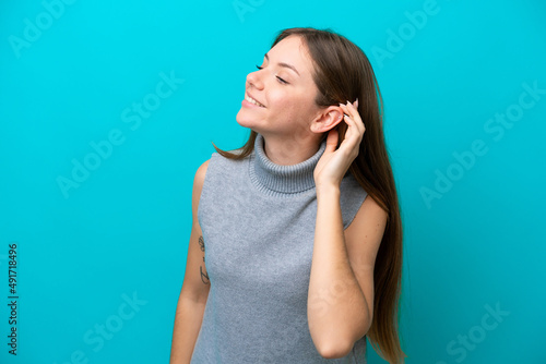 Young Lithuanian woman isolated on blue background listening to something by putting hand on the ear