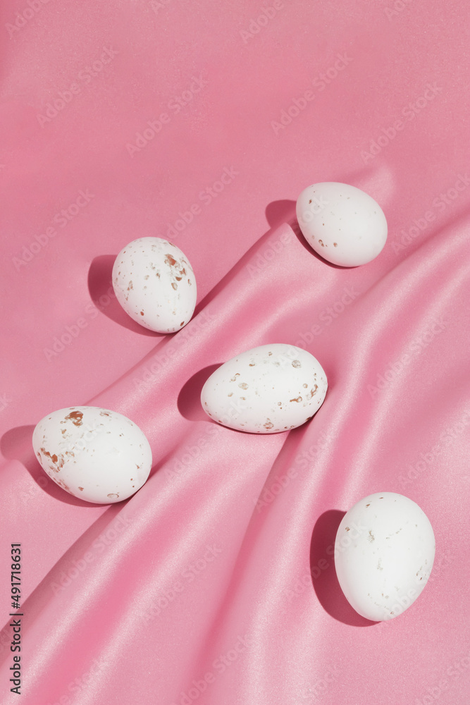 White Easter eggs on pink silk background with copy space. Easter holiday concept. Minimal flat lay composition.