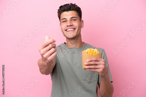 Young caucasian man holding fried chips isolated on pink background making money gesture © luismolinero