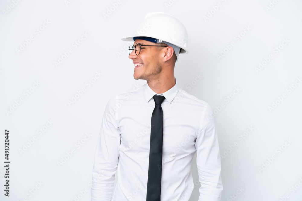 Young architect caucasian man with helmet and holding blueprints isolated on white background looking side Young architect caucasian man with helmet and holding blueprints isolated on white background looking side